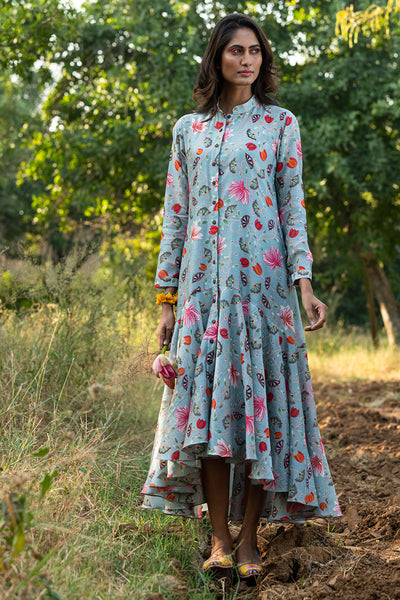 Woman wearing a floral dress standing in a natural setting with trees and grass.