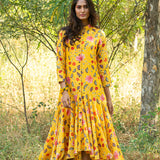 Woman in a yellow floral dress standing in a natural setting with trees and grass.