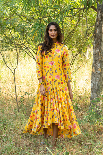 Woman in a yellow floral dress standing in a natural setting with trees and grass.