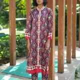 Woman wearing a patterned outfit standing in front of wooden pillars with greenery in the background
