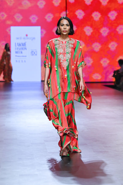 A model walking down a runway showcasing a multicolored Gulal Square Poncho with Sharara set, featuring intricate hand embroidery and a flared design.