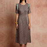 A model wearing a black and beige striped fitted dress with pleated detailing on the armholes and back, paired with yellow earrings.